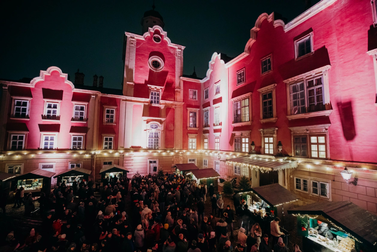 Blick über den vollen Schlosshof auf die angestrahlte Fassade mit den Marktständen davor